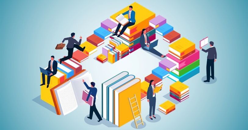 Stacks of multicolored books form a maze, with adult workers, dressed in suits, navigating up, down, and around them.