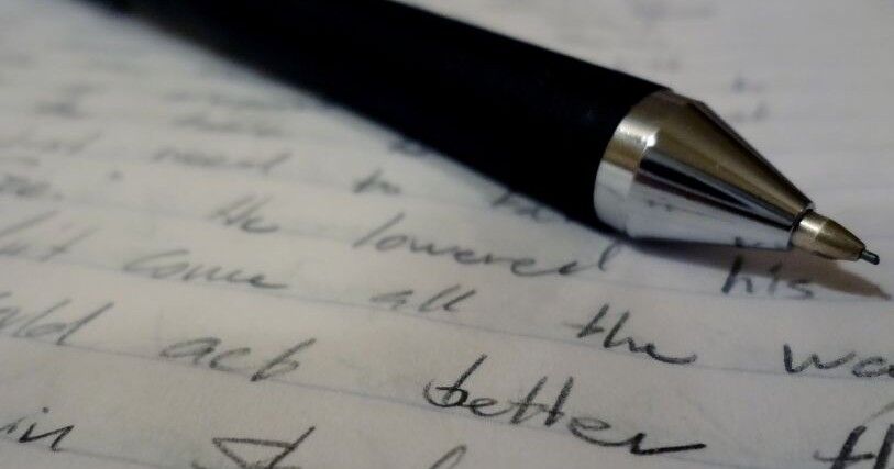 A black pen rests on a piece of paper with words in black ink