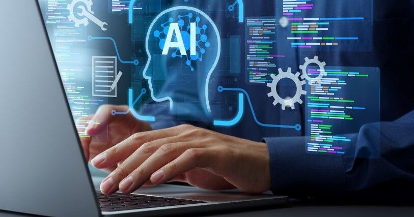 Hands hover over a laptop keyboard; above the hands are graphic images of a human head with AI superimposed, gears, and boxes with colored text boxes