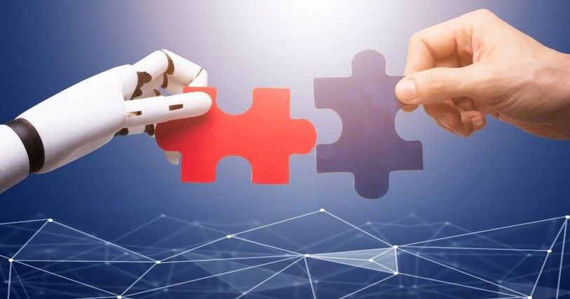 A robot hand and a human hand offer each other connecting puzzle pieces.