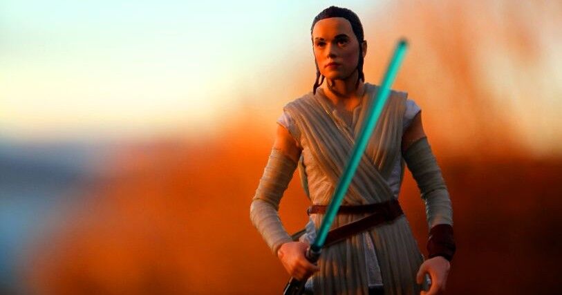 Jedi warrior Rey, emerging from a blurred orange background, holds a light saber